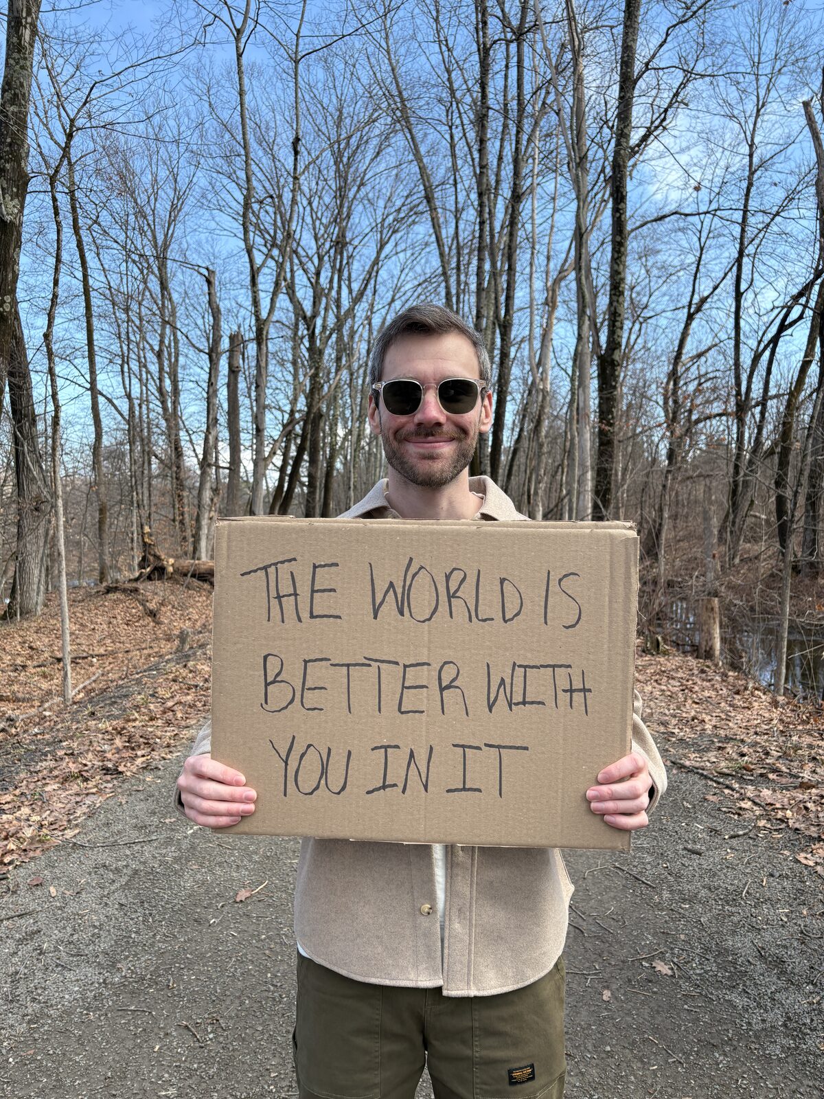 Zack holding a sign that reads: the world is better with you in it